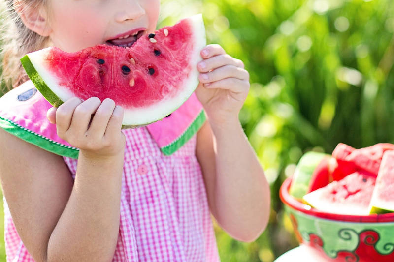 Criança comendo melancia, fruta que contribui para a hidratação do corpo.